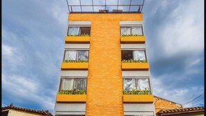 A multi-story building with a central brick facade, balconies with plants, and windows with curtains. - Comfort and style in San Javier / 15min Comuna 13 (Medellín)