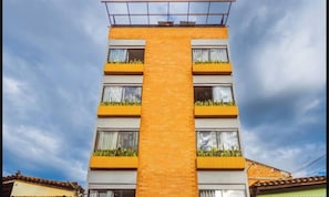 Ein mehrstöckiges Gebäude mit einer zentralen Ziegelaußenwand, Balkonen mit Bepflanzung und Fenstern mit Vorhängen.