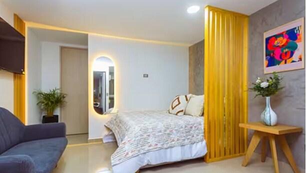 A modern bedroom with a bed, a sofa, a mirror, a wooden partition, and a painting on the wall. - Comfort and style in San Javier / 15min Comuna 13 (Medellín)