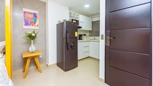 A compact kitchen with a refrigerator, a small wooden stool, and a painting on the wall. - Comfort and style in San Javier / 15min Comuna 13 (Medellín)
