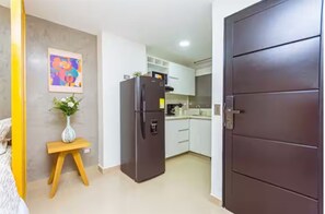 Eine kleine Küche mit einem Kühlschrank, einem kleinen Holzhocker und einem Bild an der Wand.