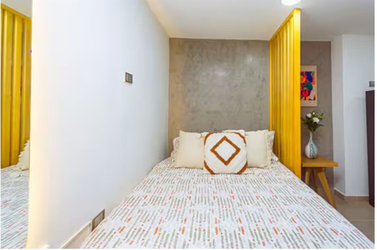 Un dormitorio con cama, mesita de noche, lámpara de pared y una vista parcial de una puerta.