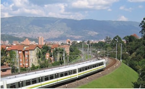 Ein Zug auf Gleisen vor einer Stadtlandschaft und Bergen im Hintergrund.