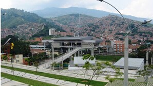 A modern building with a central staircase, surrounded by a landscaped area with trees and a clear view of a hilly cityscape in the background. - Comfort and style in San Javier / 15min Comuna 13 (Medellín)
