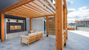An outdoor seating area with a built-in fireplace, wooden pergola, and a sofa.