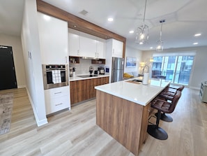Una cocina moderna con una isla central, armarios de madera, electrodomésticos de acero inoxidable y una zona de bar con taburetes.