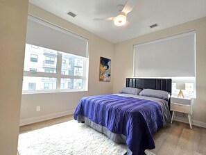 Un dormitorio con cama, ventilador de techo, ventana y mesita de noche con lámpara.