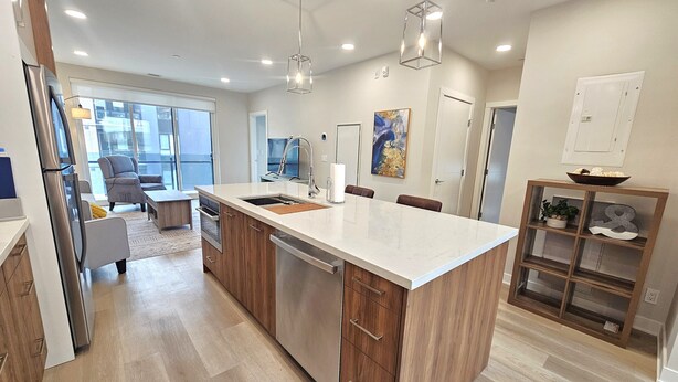 A modern kitchen with a large island, wooden cabinets, stainless steel appliances, and pendant lighting.