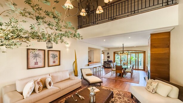 A spacious living area with a high ceiling, a dining area with a glass table, and a balcony with a railing.