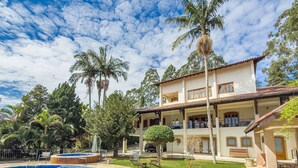 A two-story house with a swimming pool, surrounded by palm trees and a well-maintained lawn.
