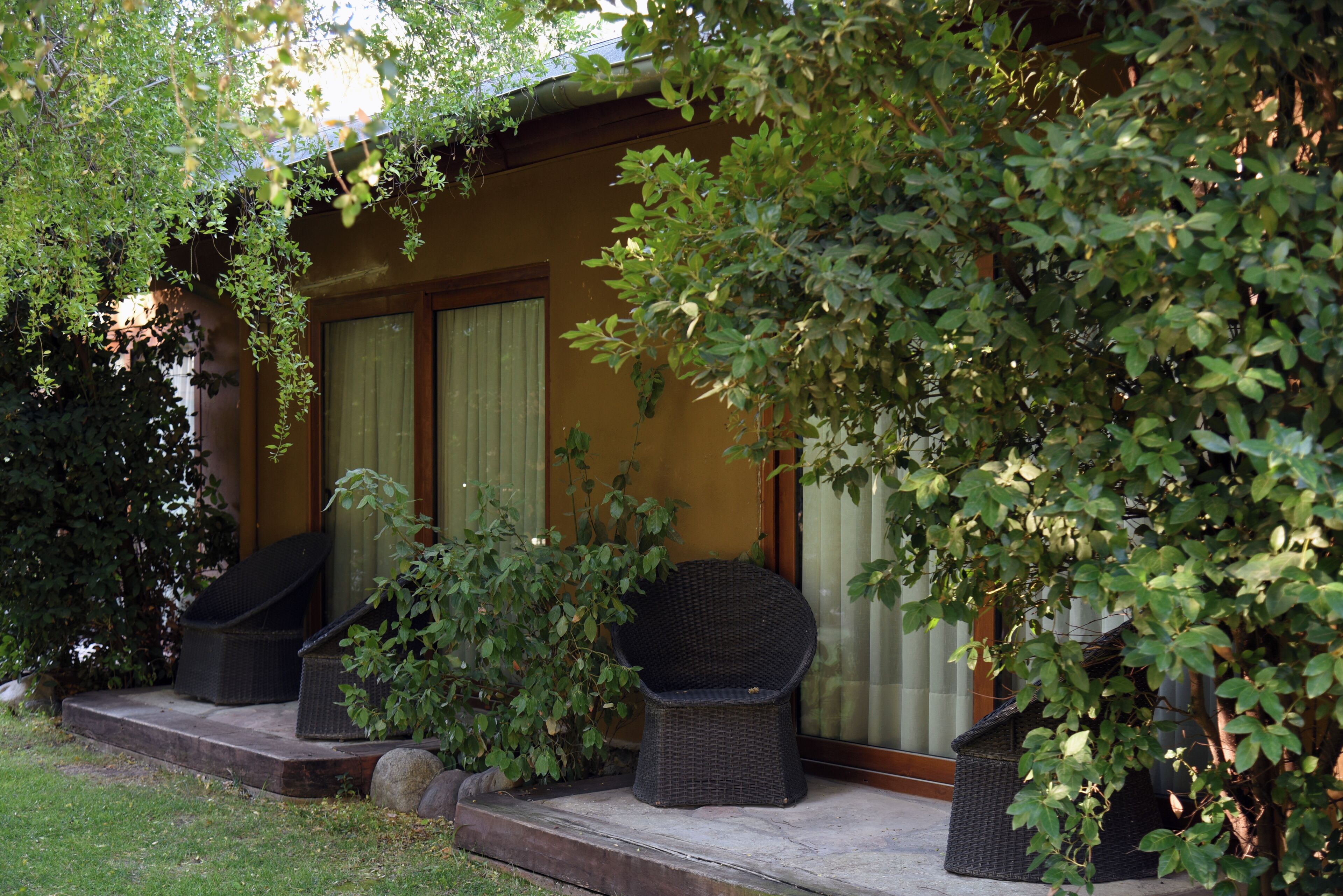 Un bâtiment doté d’un porche, de deux fauteuils en osier et d’un petit jardin.