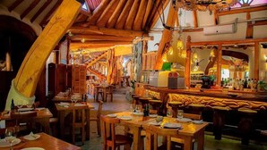Ein Restaurant mit Holztischen, einer Bar und einer hohen Decke mit freiliegenden Balken.