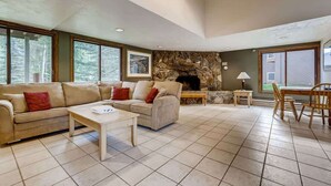 Ein geräumiges Wohnzimmer mit Kamin aus Stein, einer Sofagarnitur, einem Couchtisch und einem Essbereich mit Tisch und Stühlen.