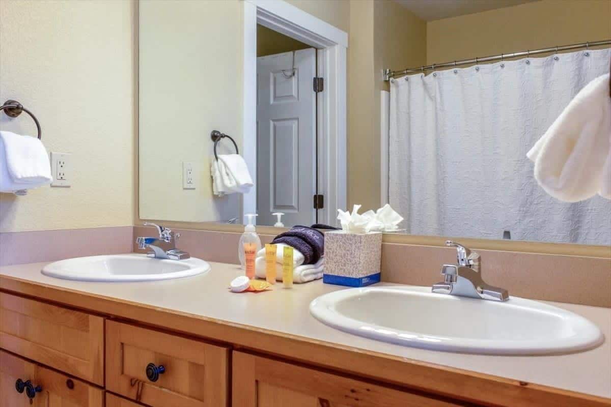 Une salle de bain avec deux lavabos, un miroir, un porte-serviettes et un rideau de douche.