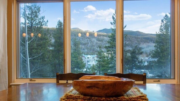 A dining table with a wooden bowl centerpiece, three windows with a forest view, and a chair. - Fun and Relaxation in a Mountain Vacation Getaway! (Keystone)