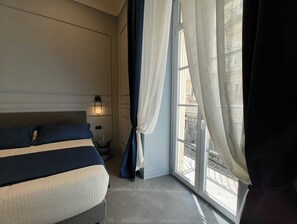 Ein Hotelzimmer mit einem Bett, einem Nachttisch, einer Wandleuchte und einem Fenster mit Vorhängen.