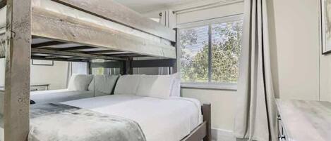 A bunk bed room with a window, a desk, and a chair.