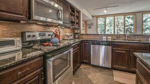 A modern kitchen with stainless steel appliances, dark wood cabinets, and a large window providing a view of trees. - Close to Slopes, Pool, & Nature: The Pines Condo in Beautiful Keystone (Keystone)