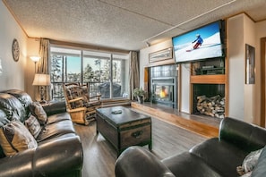 Ein Wohnzimmer mit Kamin, Fernseher und Blick ins Freie.