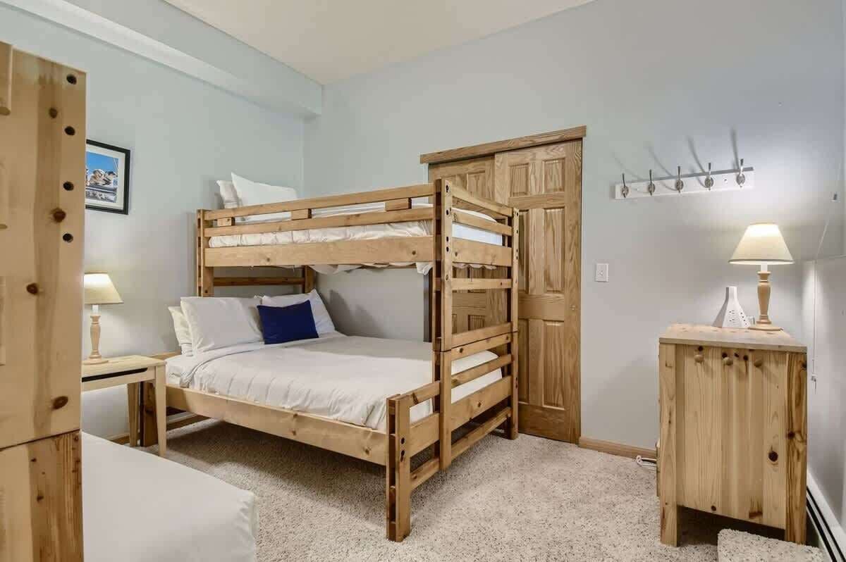 Una cama litera con estructura de madera, una mesita de noche pequeña, una lámpara y un pequeño tocador.