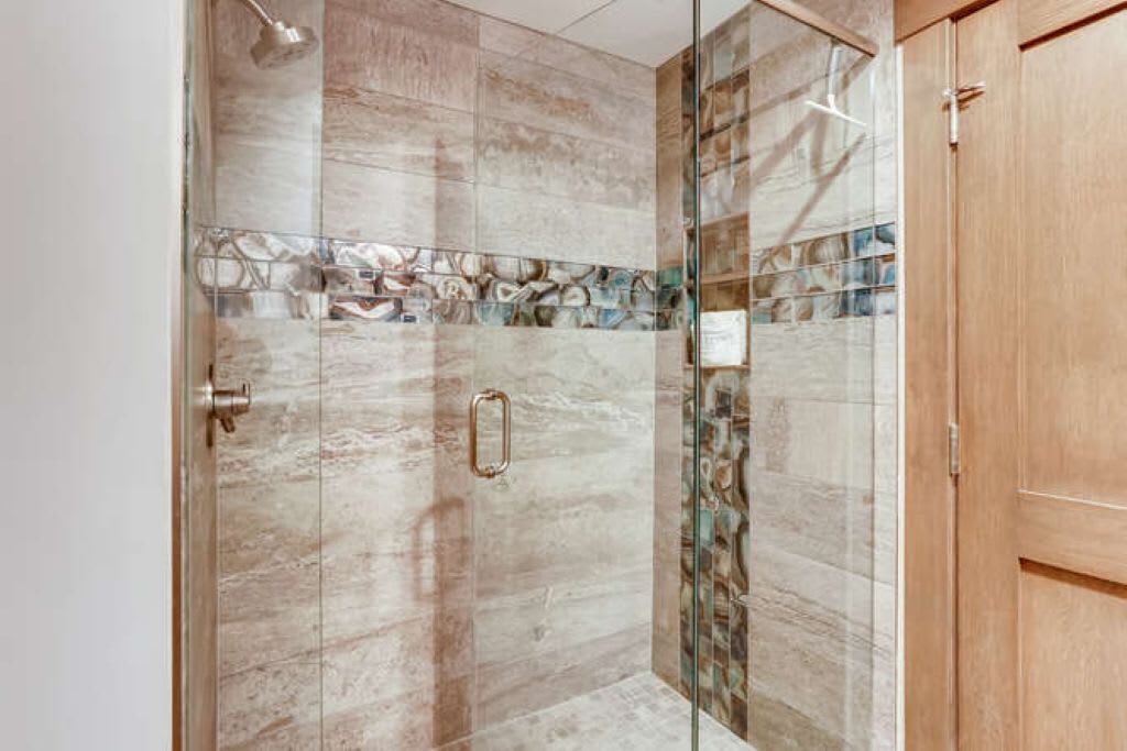 A glass-enclosed shower with a marble wall and a wooden door.