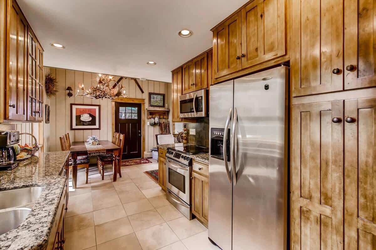 Cucina con mobili in legno, elettrodomestici in acciaio inossidabile, zona pranzo con lampadario e un quadro appeso al muro.