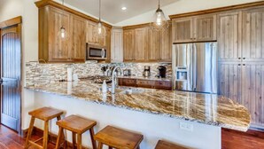 A kitchen with wooden cabinets, granite countertops, and bar stools. - Amazing Heart of Frisco Condo (Frisco)