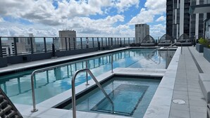 Ein Pool auf dem Dach mit freiem Blick auf die Stadtlandschaft, ein kleines Whirlpool und eine Sitzecke mit Kissen.