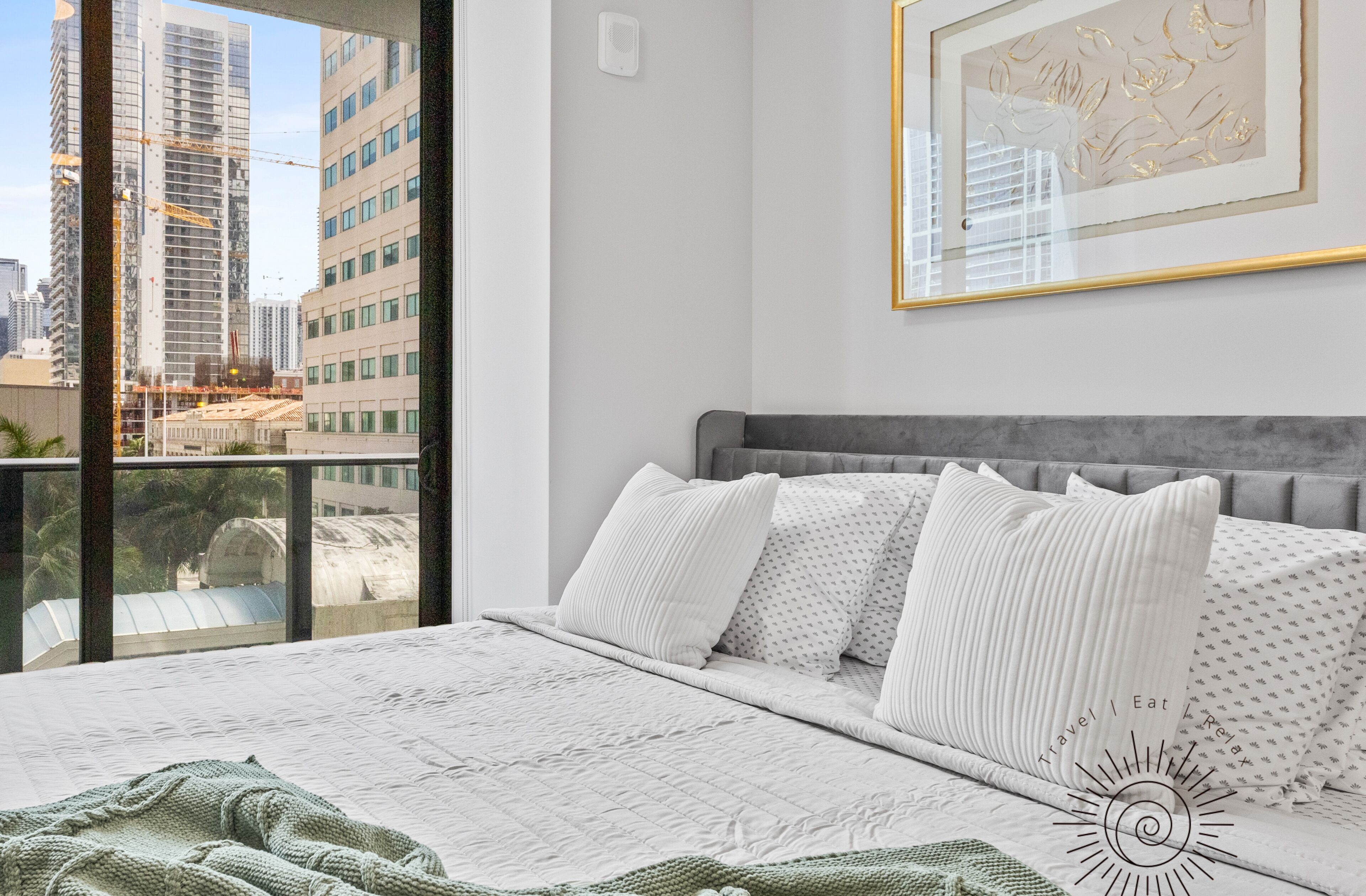A bedroom with a large bed, a grey headboard, white bedding, and a framed artwork on the wall.