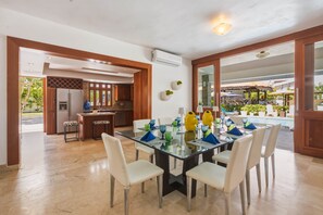A dining area with a glass table, white chairs, and a view of the outdoor pool. - Villa Bella Laguna | Beach Access (Sosúa)