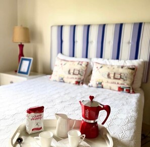 A neatly made bed with a striped headboard, a bedside lamp, and a tray with a coffee pot, cups, and a packet of coffee. - Villa Bella Laguna | Beach Access (Sosúa)