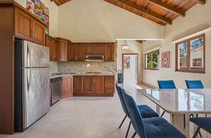 Eine moderne Küche mit Holzschränken, einem Edelstahlkühlschrank, Granit-Arbeitsplatten und einem Essbereich mit blauen Stühlen.