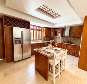 A kitchen with wooden cabinets, a stainless steel refrigerator, a central island with chairs, and a skylight. - Villa Bella Laguna | Beach Access (Sosúa)
