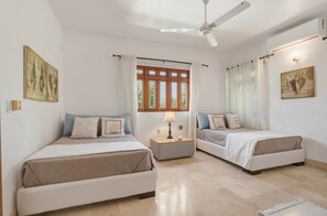 Ein Schlafzimmer mit zwei Betten, einem Deckenventilator, einem Nachttisch mit Lampe und einem Fenster mit Vorhängen.
