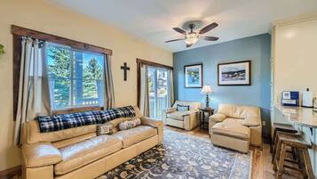 A living room with a sofa, two chairs, a coffee table, a ceiling fan, and a large window with curtains.