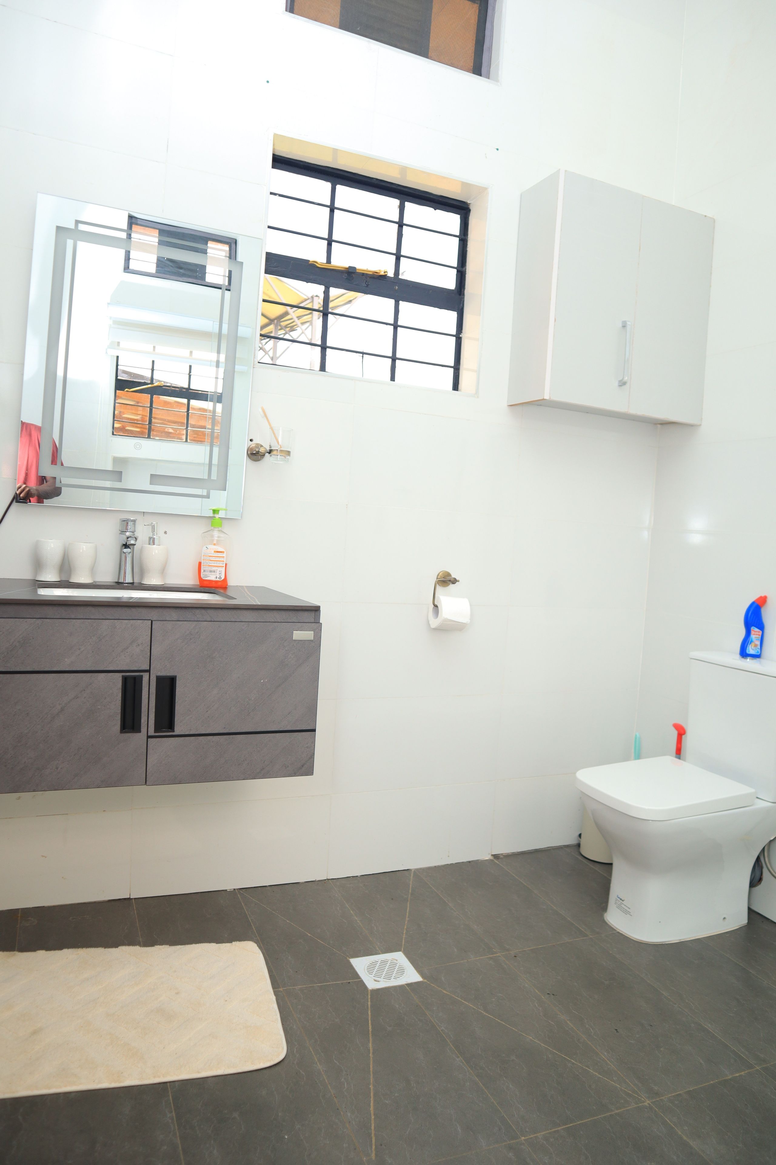 Ein modernes Badezimmer mit grauem Waschtisch, einer weißen Toilette und einem Fenster mit Metallgitter.