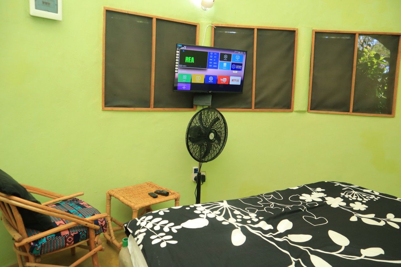 A room with a bed, a chair, a small table, a TV mounted on the wall, and a fan.