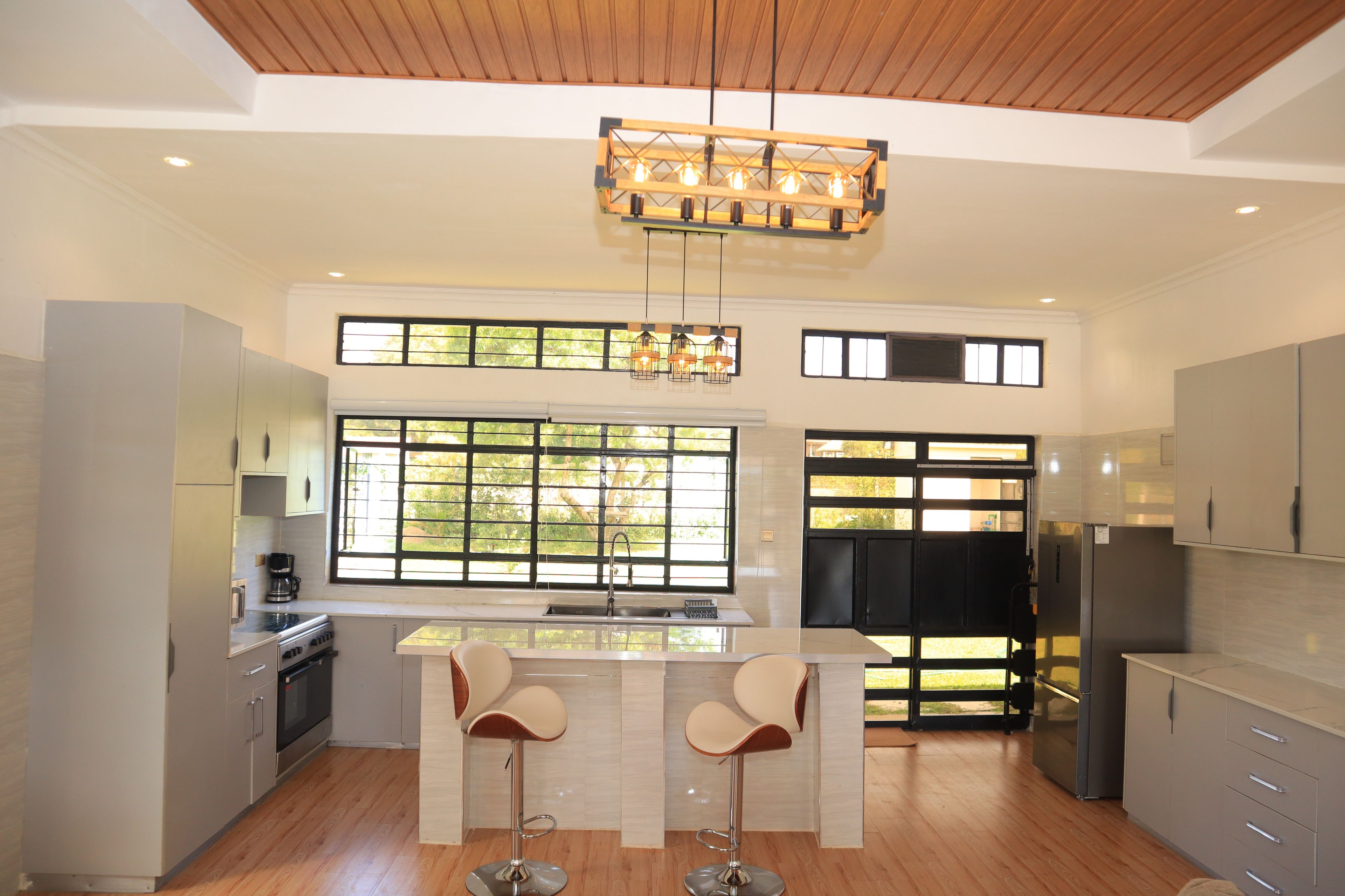 A modern kitchen with a central island, bar stools, a built-in oven, and a large window providing natural light.