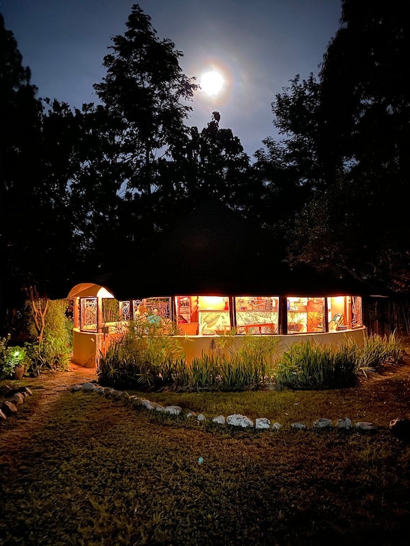 A building with a glass facade, surrounded by trees and illuminated by ambient lighting.