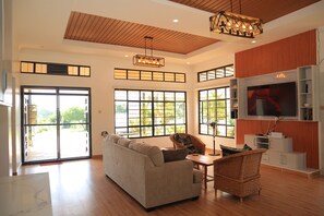 Un salón espacioso con sofá, sillón de mimbre, televisor y ventilador de techo.