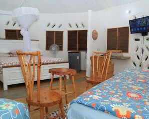 A room with a bed, a chair, a small table, a fan, and a television.