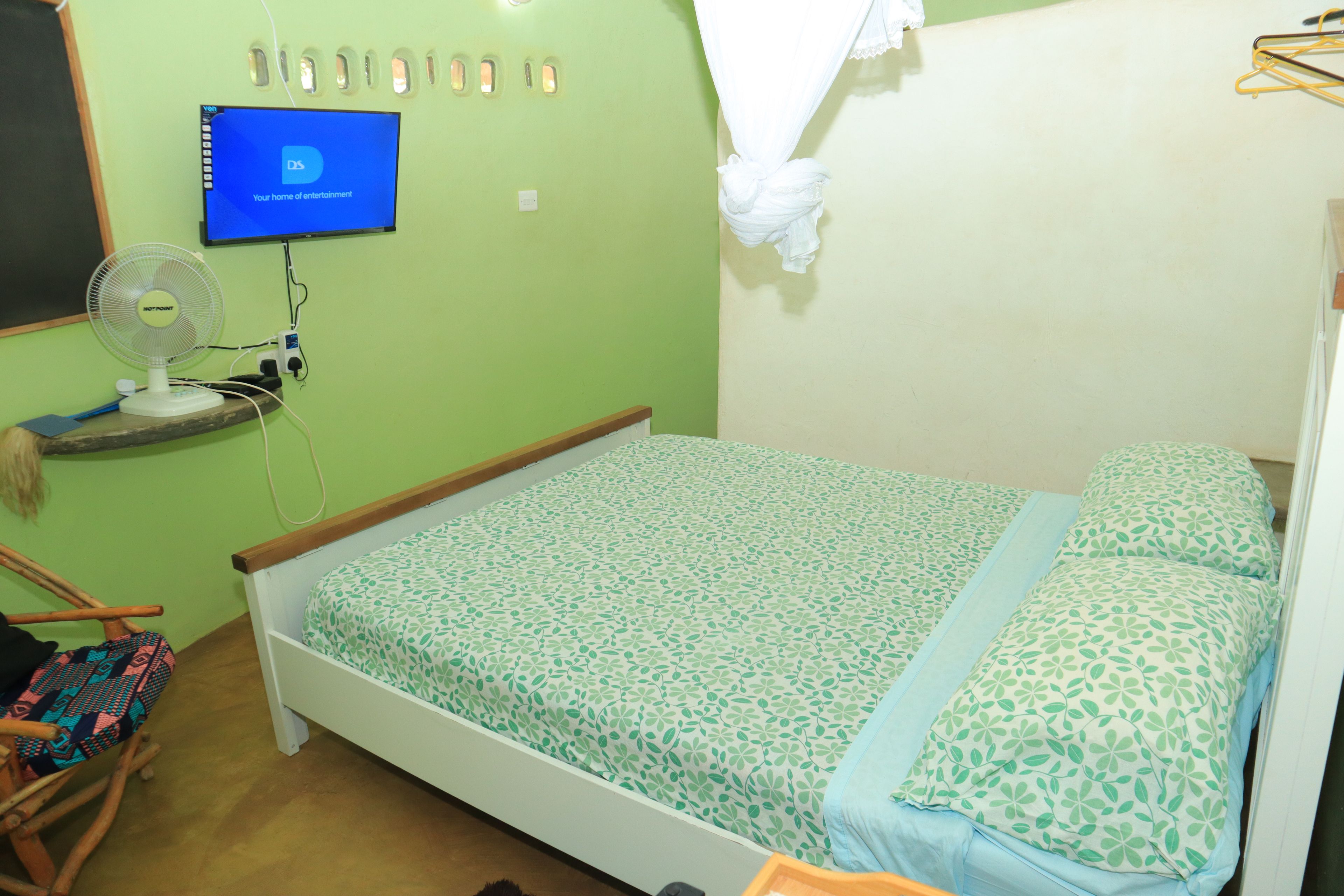 Una habitación con cama, ventilador, televisor y lámpara de pared.