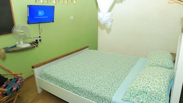 Una habitación con cama, ventilador, televisor y lámpara de pared.