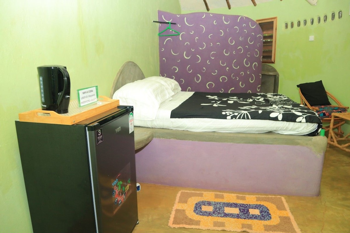 Una habitación pequeña con una cama, un escritorio con cafetera y un refrigerador.