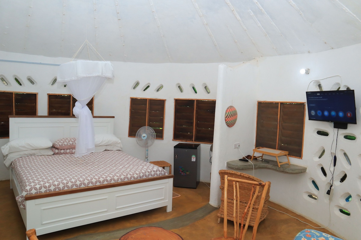 Un dormitorio con cama, ventilador, una mesita y televisor.
