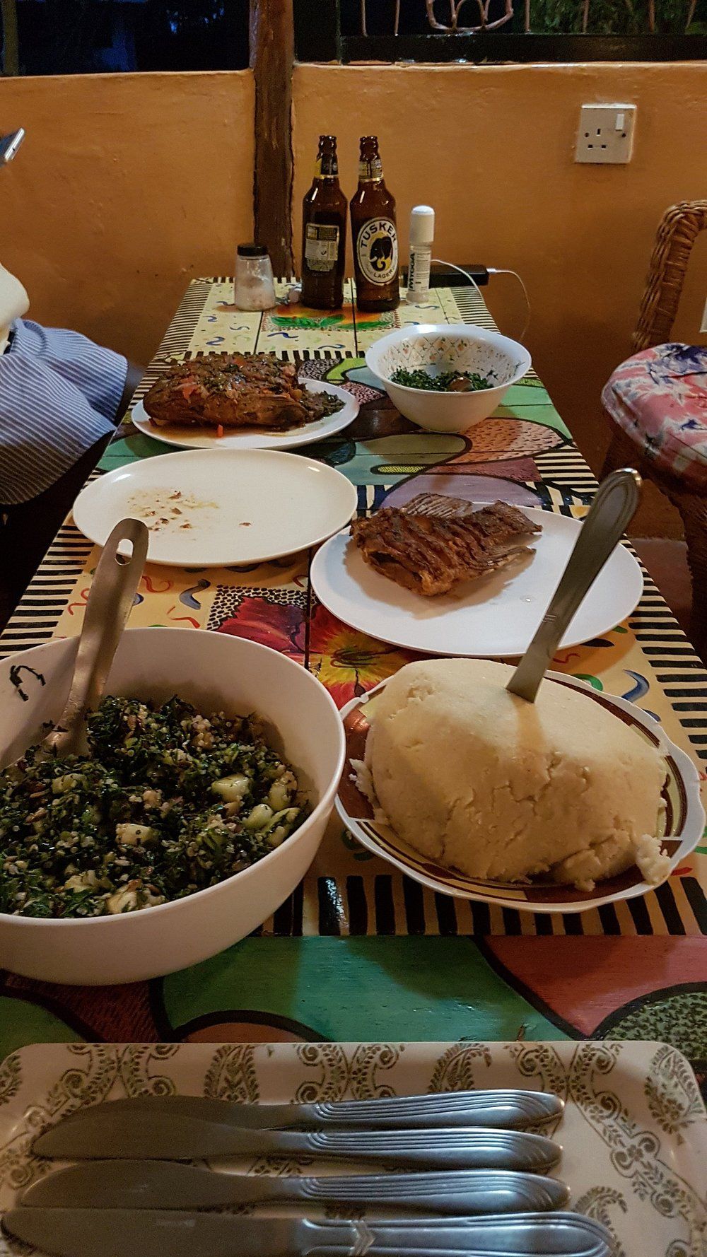 A dining table with various dishes, including a bowl of salad, a plate of meat, and a bowl of mashed potatoes. There are also bottles and a bowl of soup on the table.