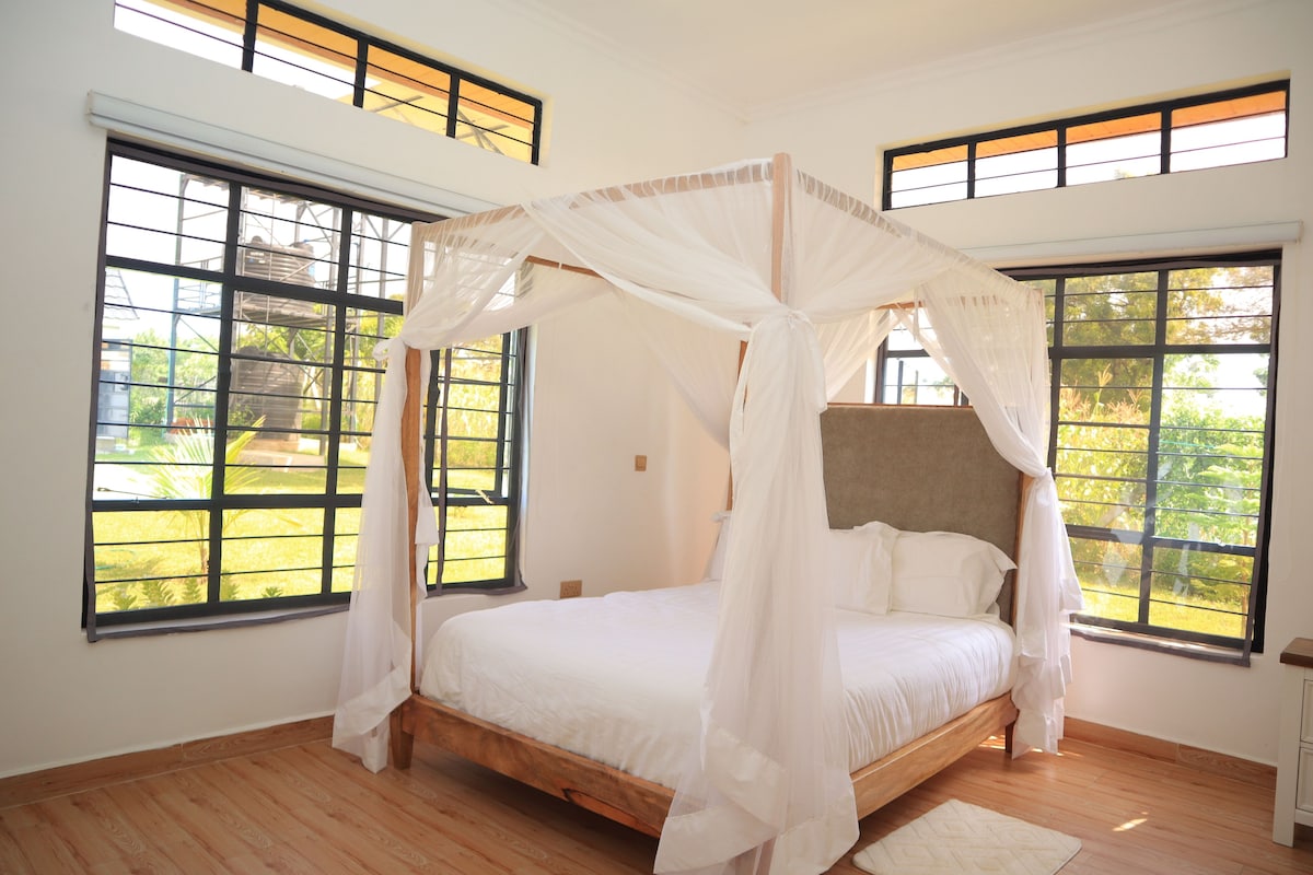 Un dormitorio con cama con dosel, ventanas amplias y suelo de madera.