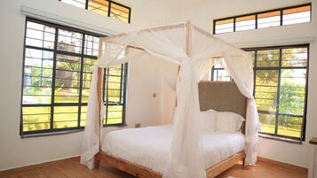 A bedroom with a four-poster canopy bed, large windows, and wooden flooring.