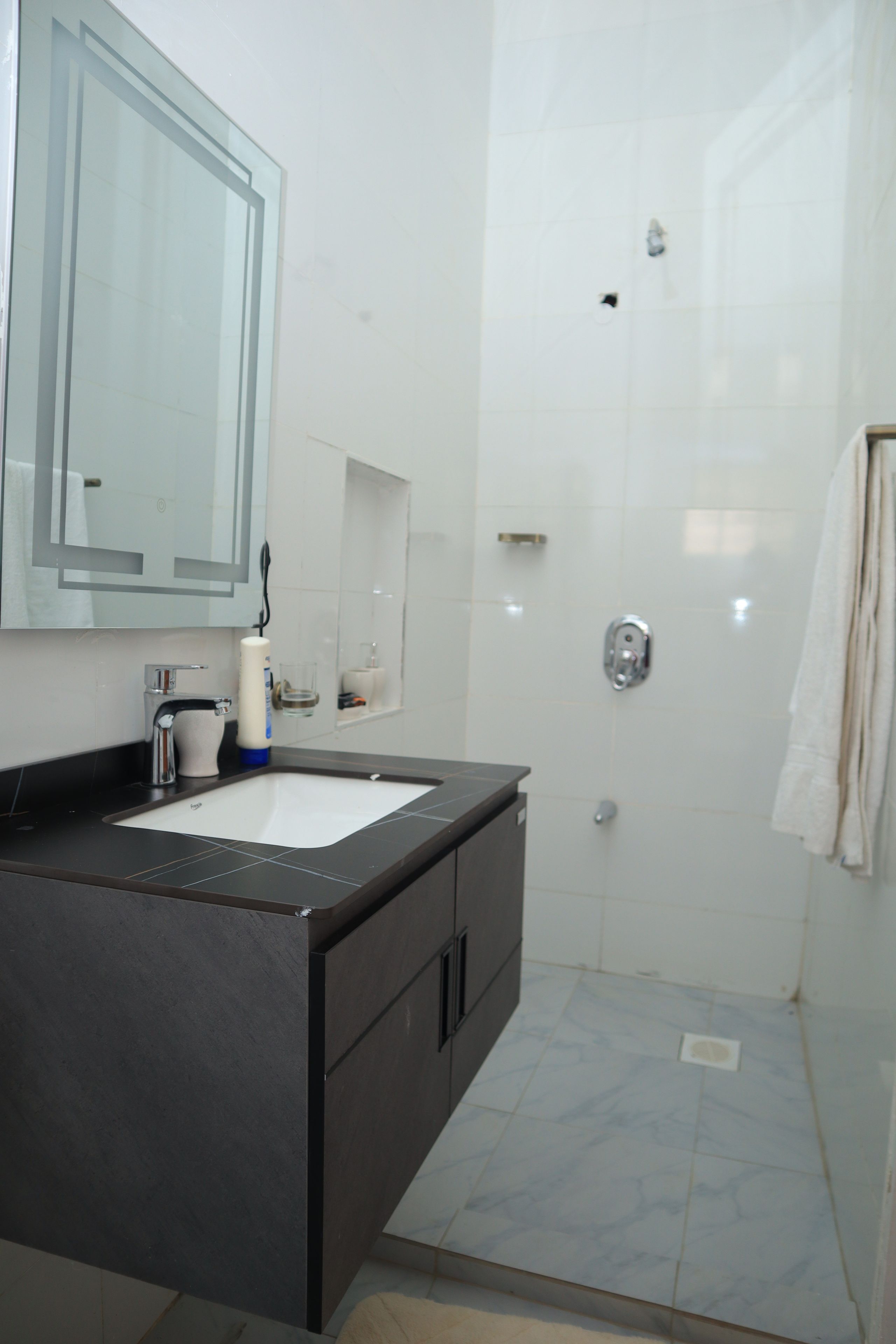 A bathroom with a dark countertop, a white sink, a mirror, and a shower area.