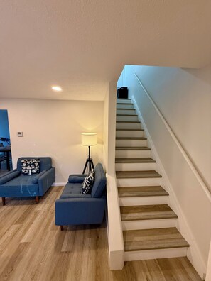 Una sala de estar con una escalera, un sofá, una lámpara y un comedor.